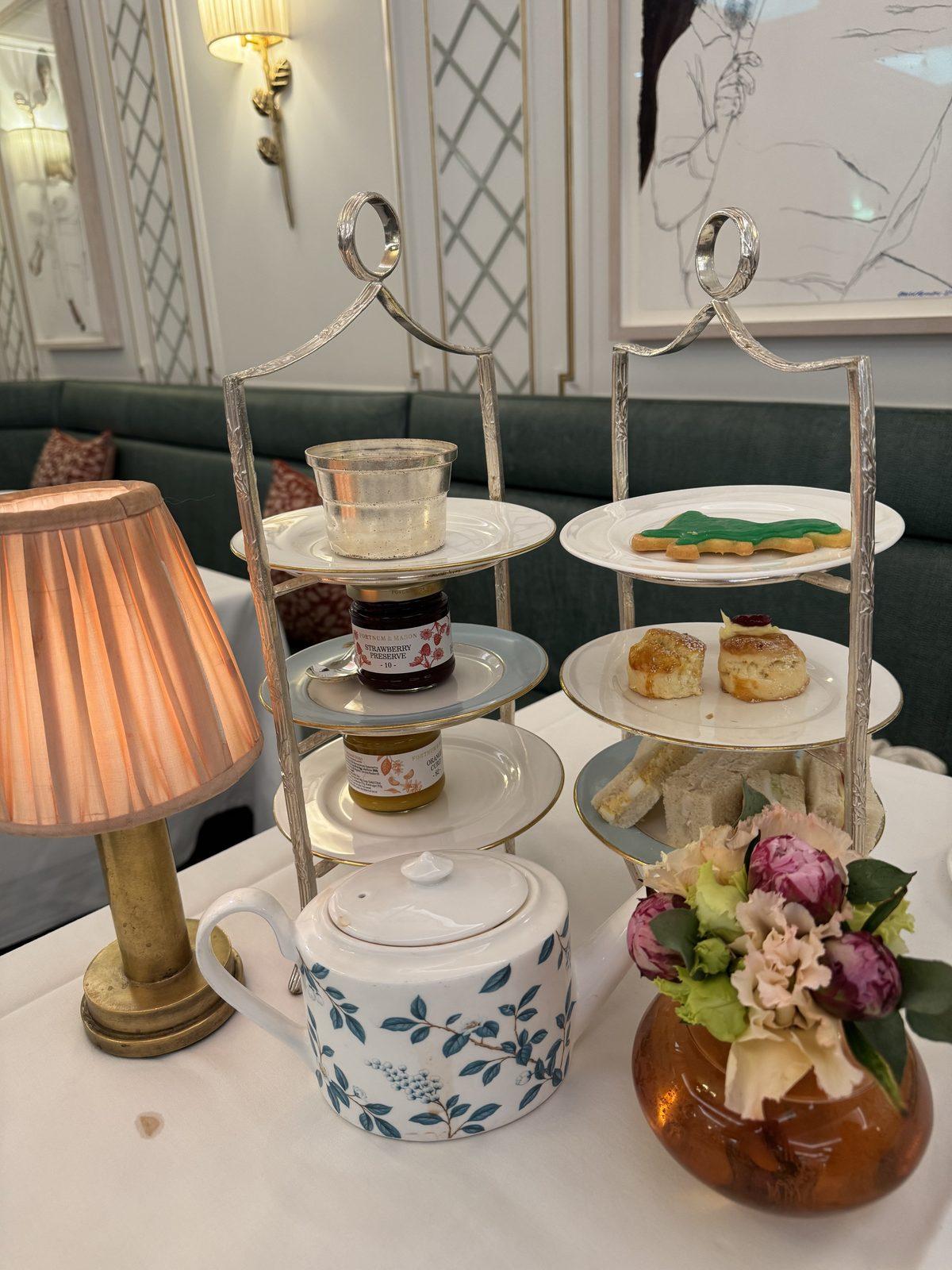 An afternoon tea stand with pastries, a teacup and a small lamp