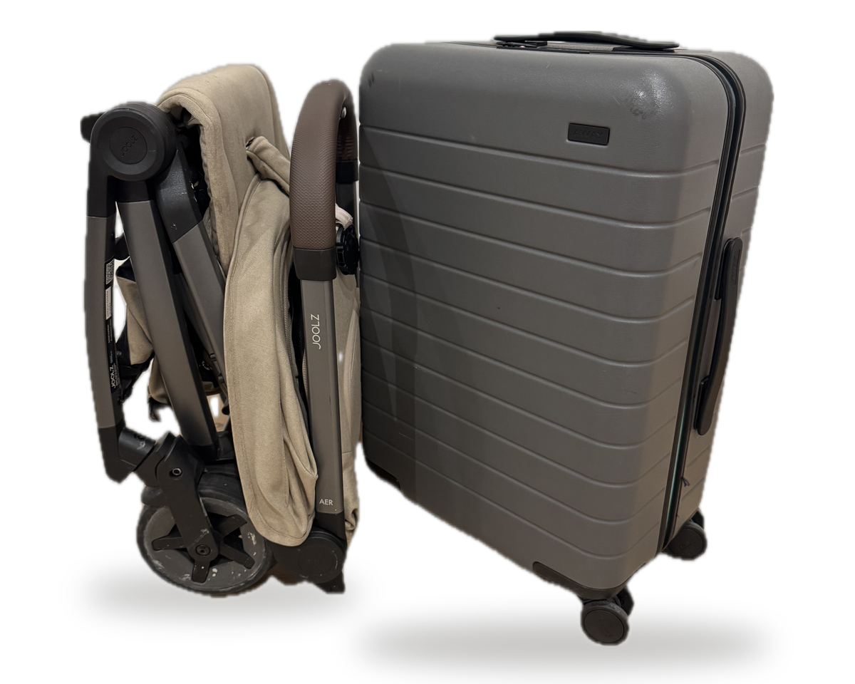 Our folded stroller standing beside our grey hardside carry-on, the stroller noticeably the smaller of the two