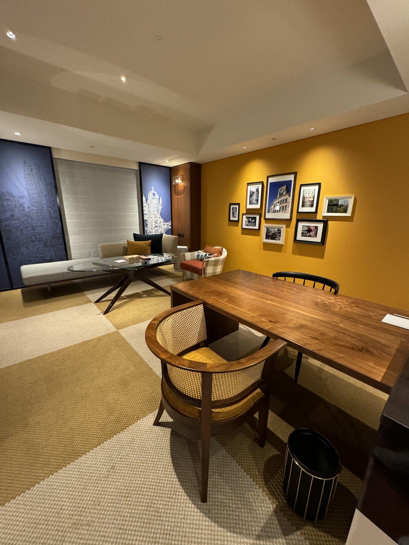 A hotel suite living area with a mustard accent wall, a framed photo gallery, and a lounge seating area