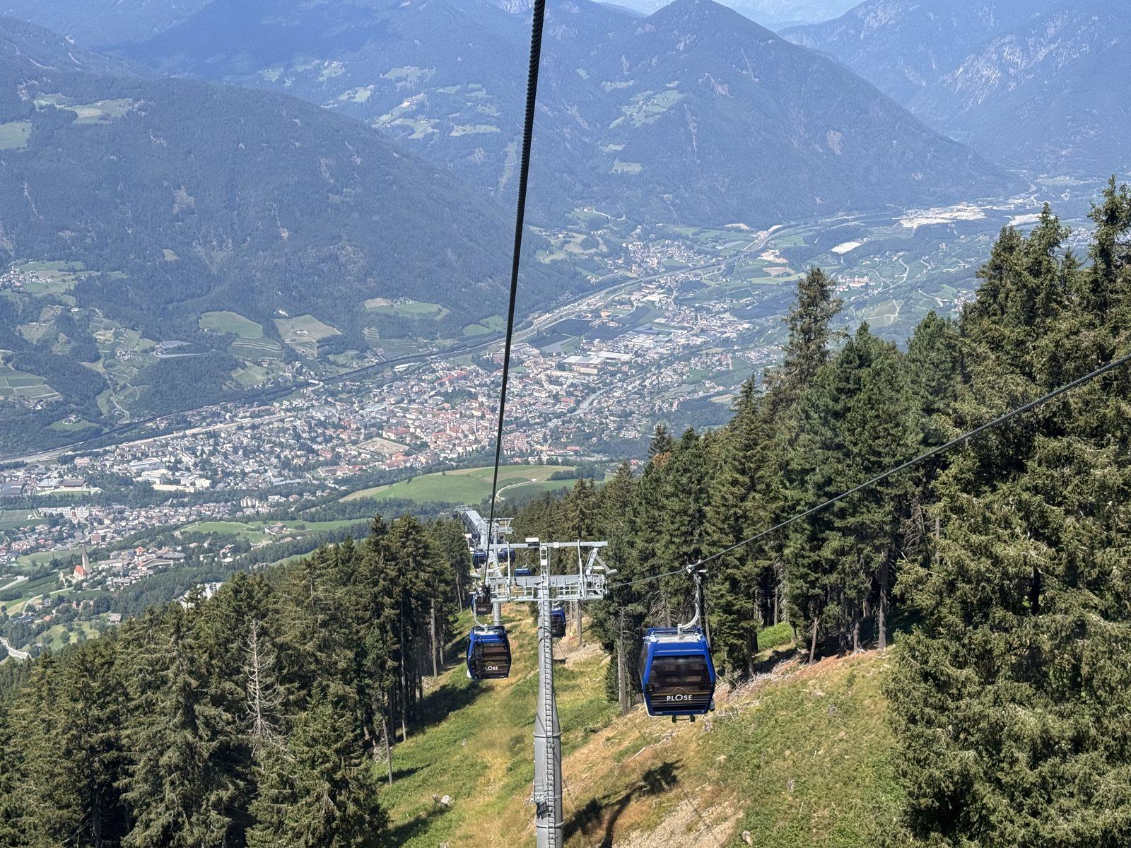 A cable car climbing above a green valley in South Tyrol