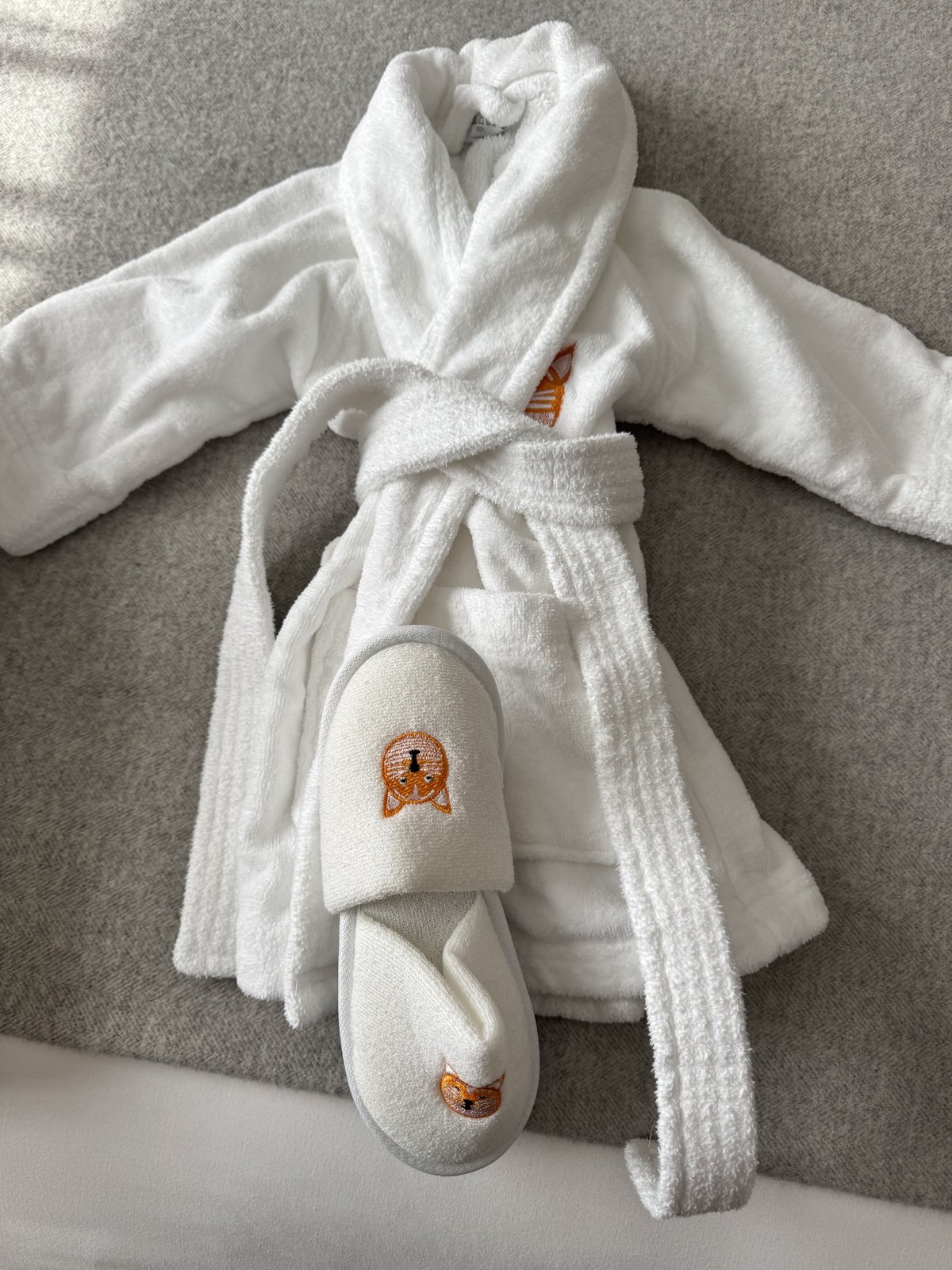 A kid-sized white robe and slippers with an embroidered animal design