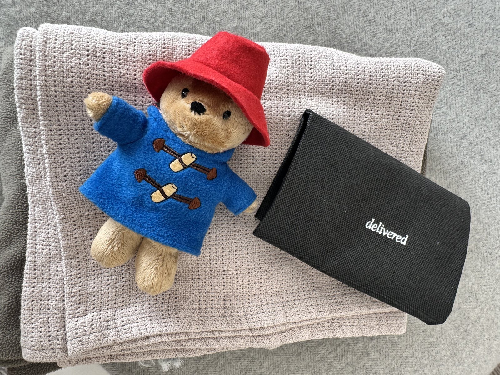 A Paddington Bear plush toy next to a hotel welcome pouch