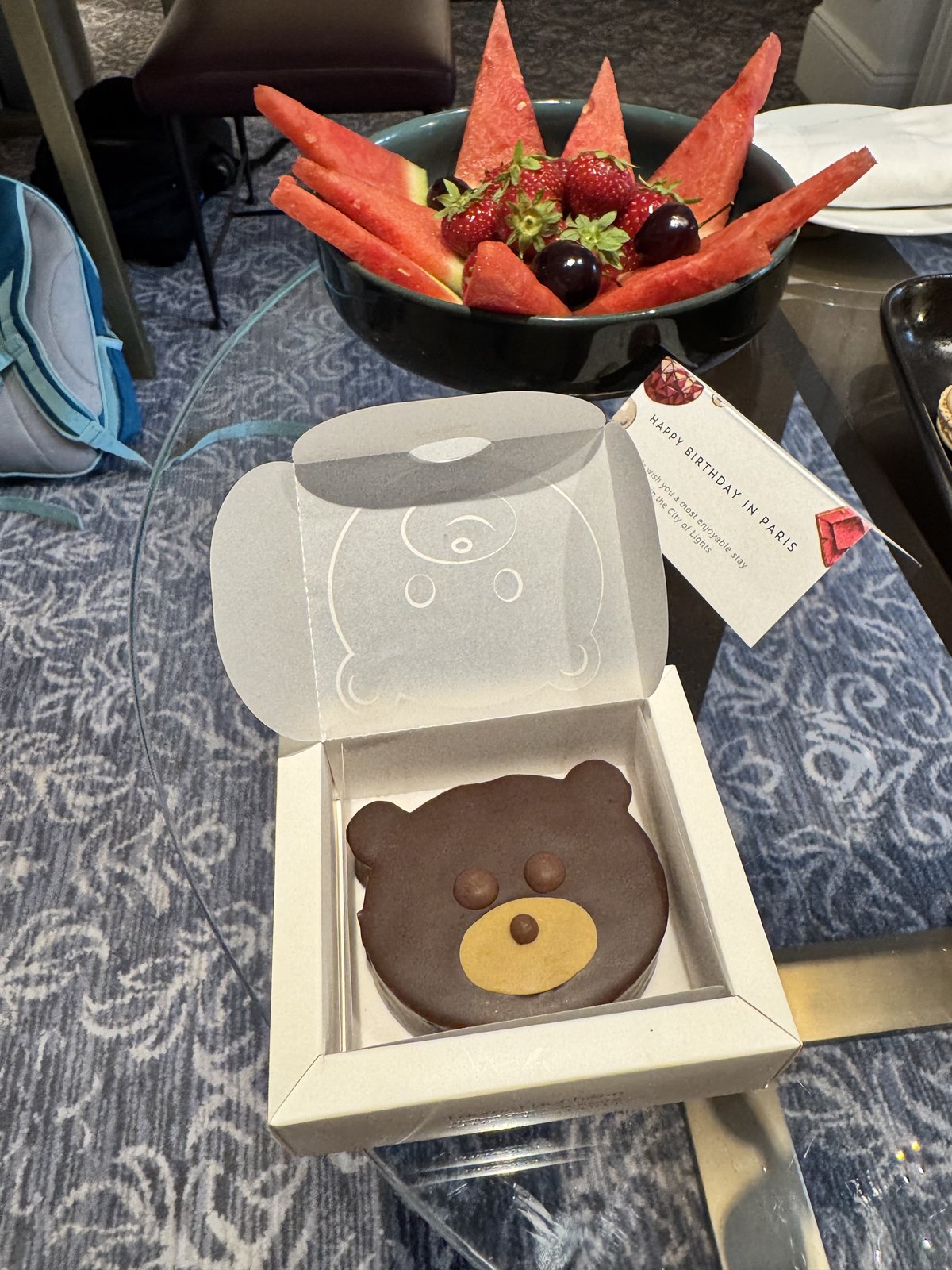 A bear-shaped chocolate cake in a gift box on a hotel room table