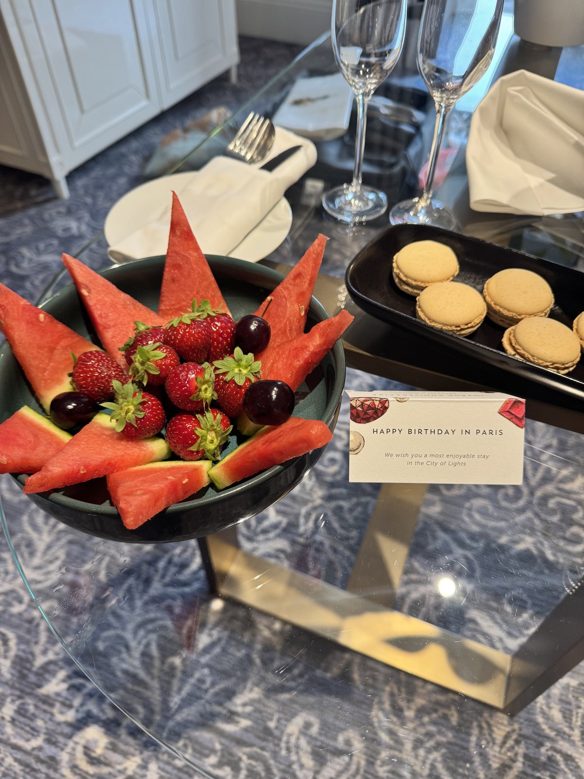 A fruit platter and a plate of macarons on a hotel room table, next to a birthday welcome card